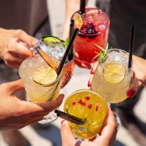 Five exotic cocktails on ice in hands joined in celebratory toast